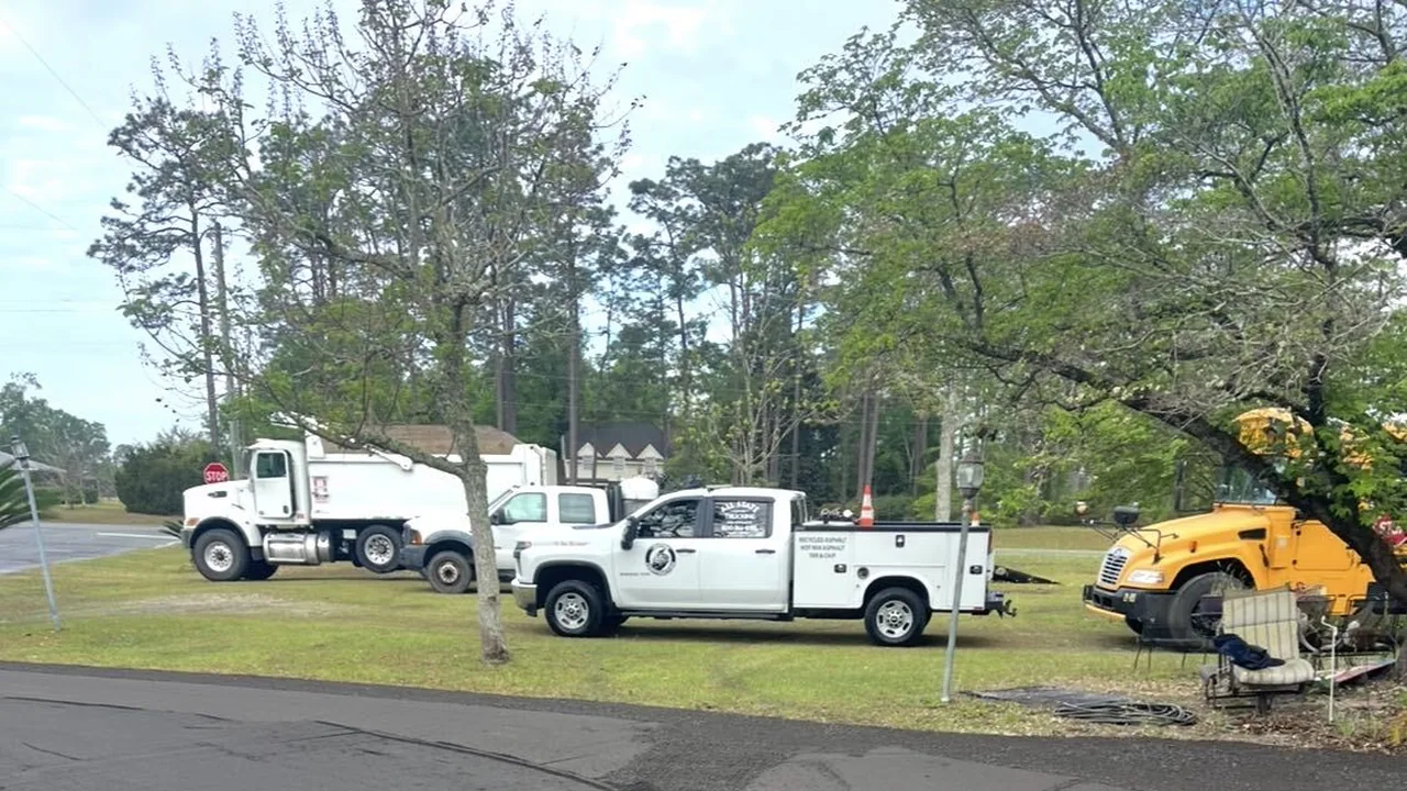 Dump truck and work pickups parked on a grass lot, asphalt paving