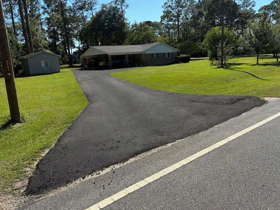 Freshly paved curved drive with a wide apron at the road to a brick home, asphalt driveways
