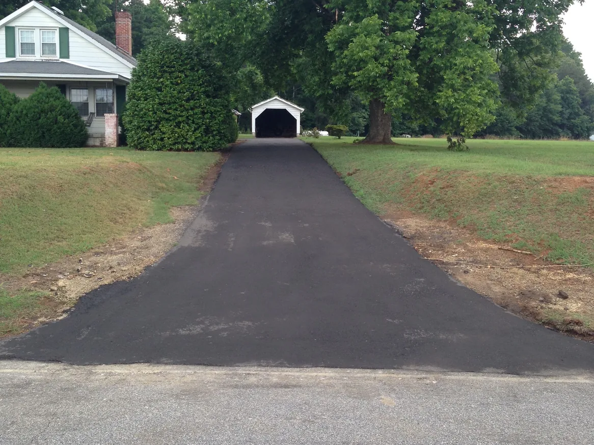 Freshly paved drive leading up to a small garage beside a home, asphalt driveways