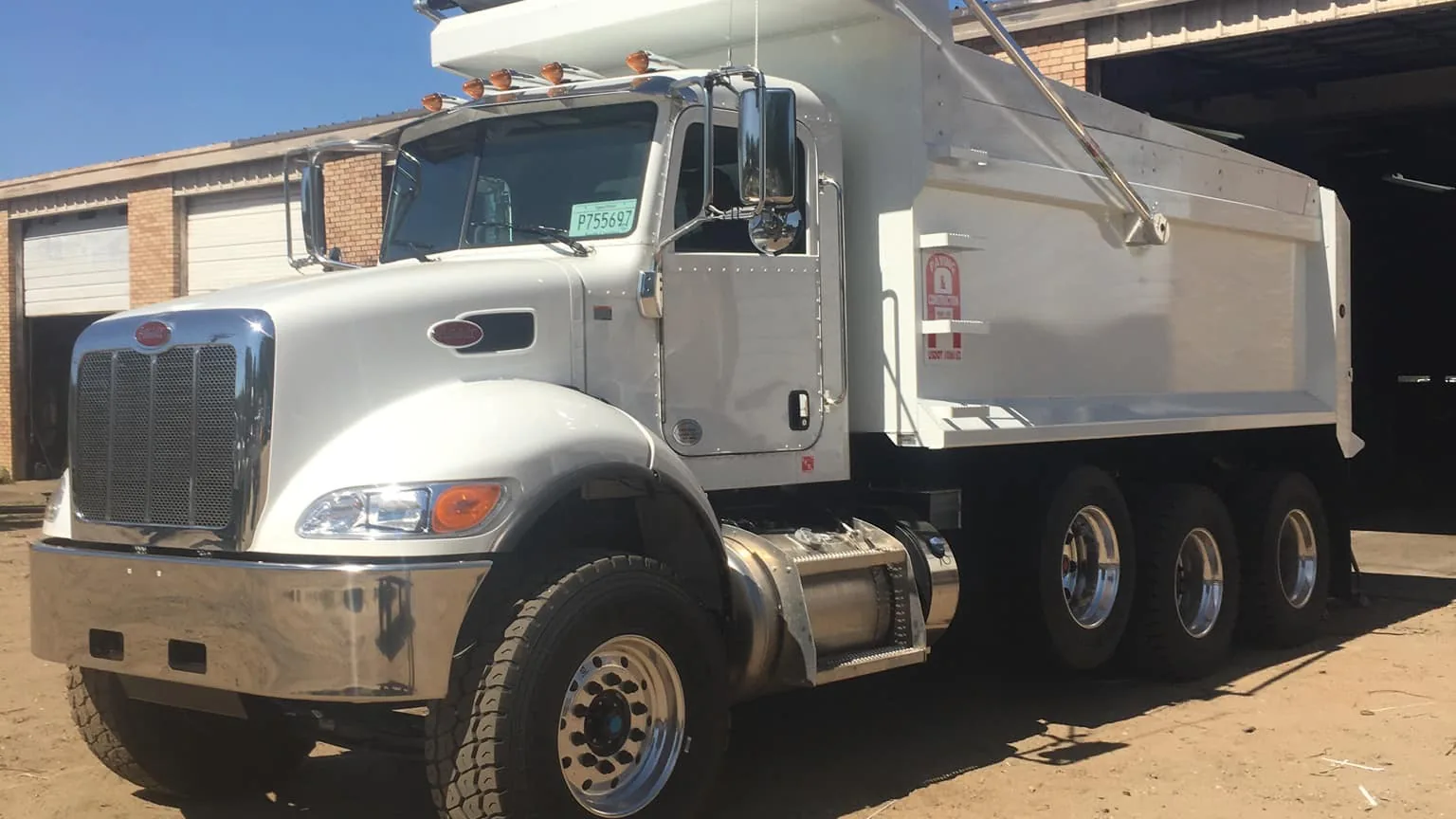 White tri axle dump truck parked by a shop building