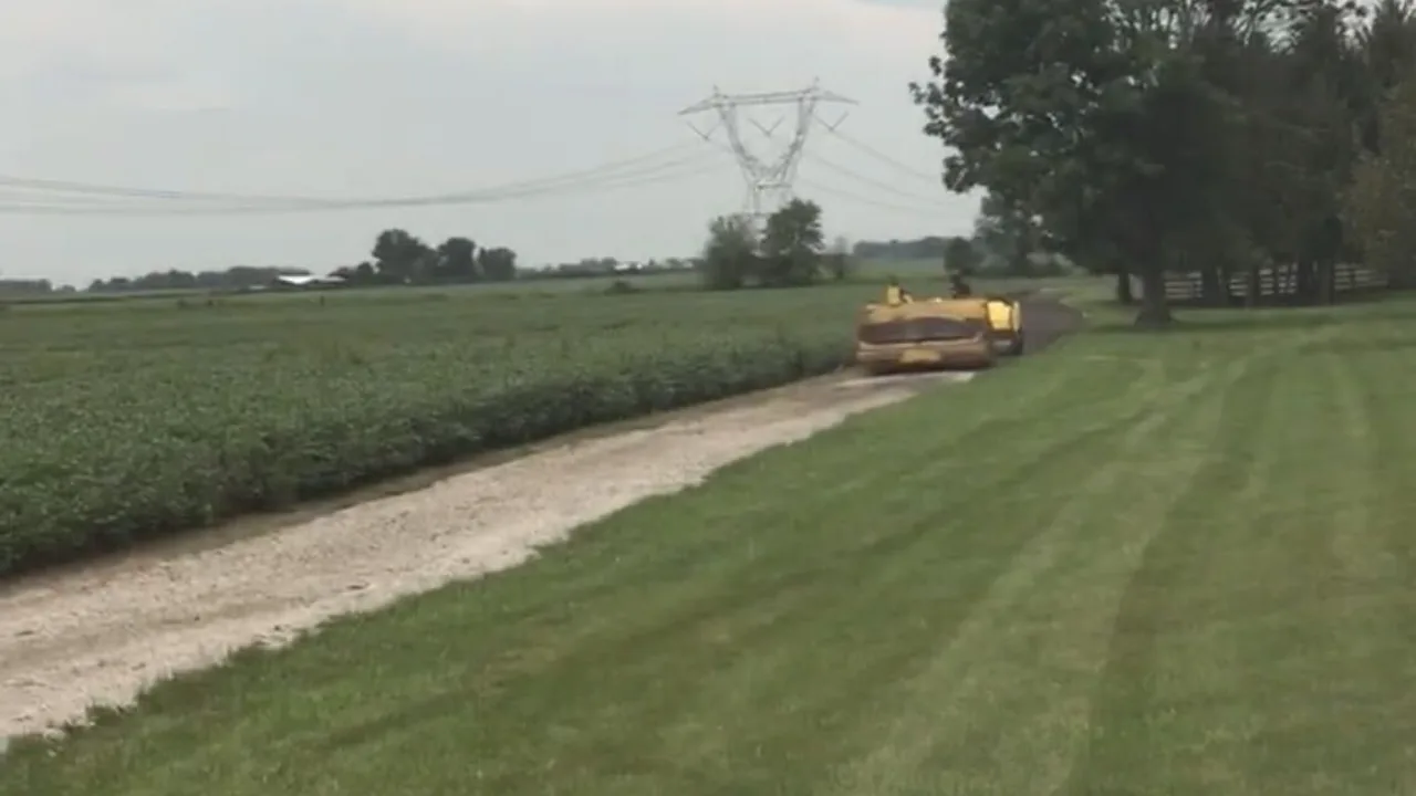 Paving machine surfacing a gravel farm lane beside a crop field
