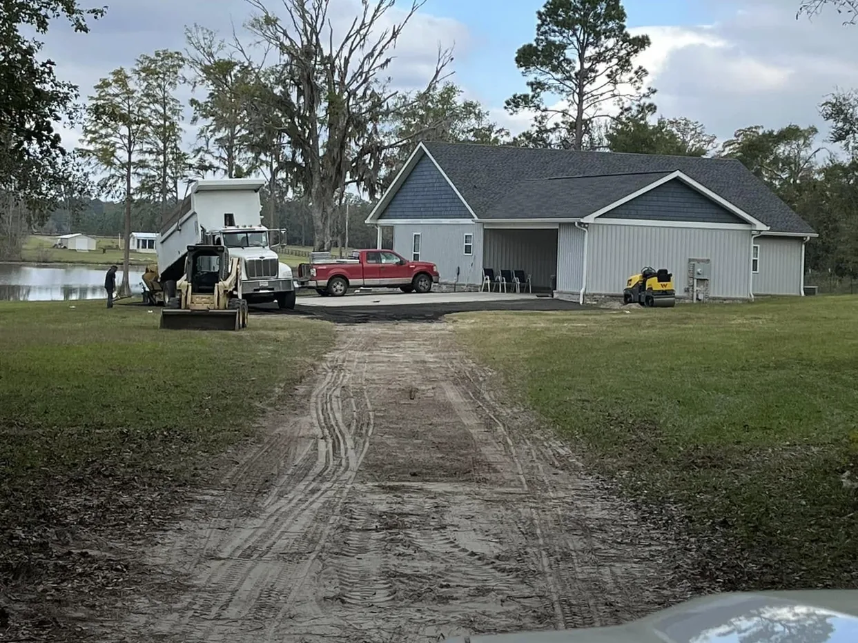 Graded dirt drive leading to a new home with a dump truck, skid steer and roller on site, grading