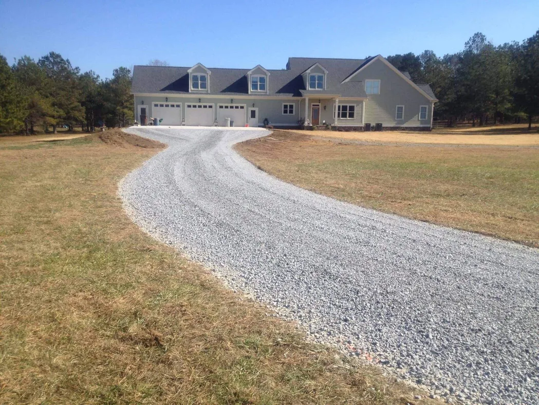 New gravel drive curving up to a house with freshly graded soil shoulders, grading