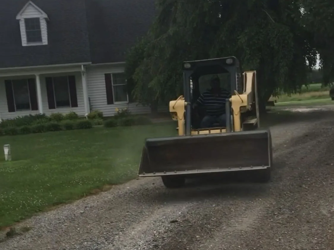 Skid steer working a gravel drive beside a house, gravel driveways