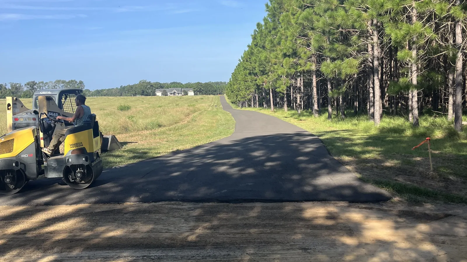 Asphalt paving contractor vibratory roller on a freshly paved long drive lined with pines