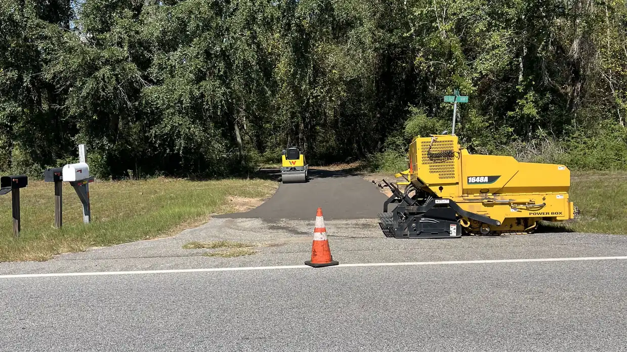 Paving machine and roller at a freshly paved driveway entrance off the highway, our work in recycled asphalt