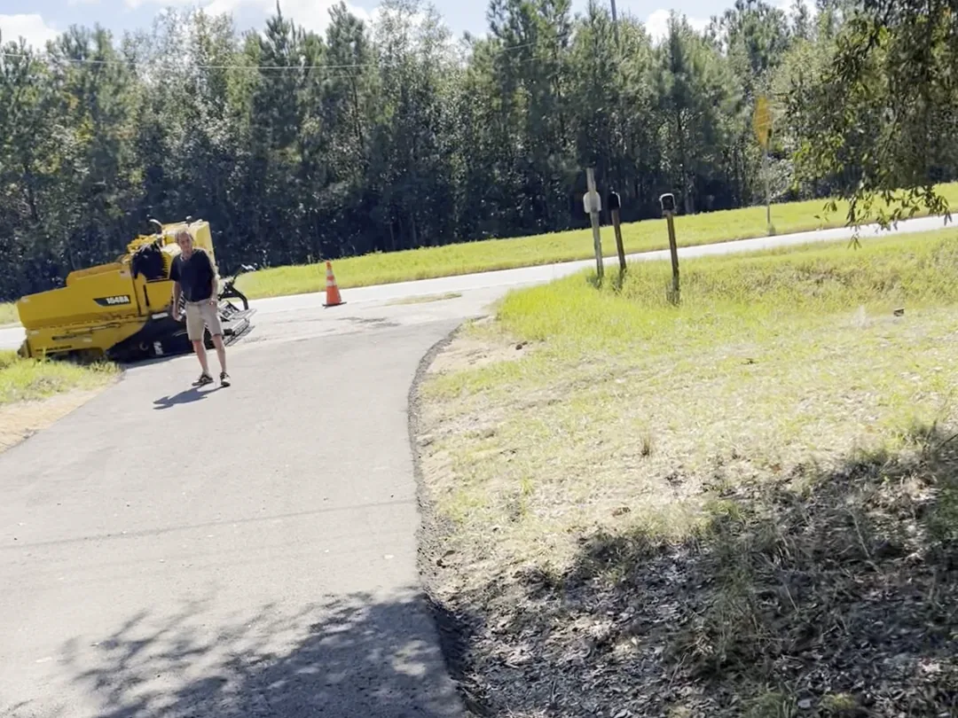 Paving machine and crew at the finished road entrance where it meets the pavement