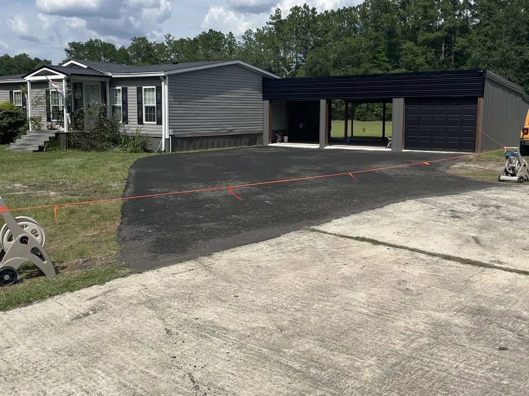Freshly paved parking pad in front of a home and a metal carport, parking lot paving