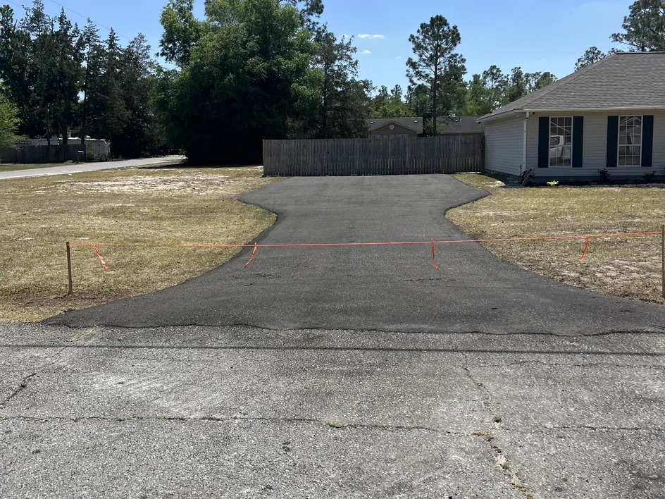 Freshly paved parking pad with a wide apron beside a home, parking lot paving