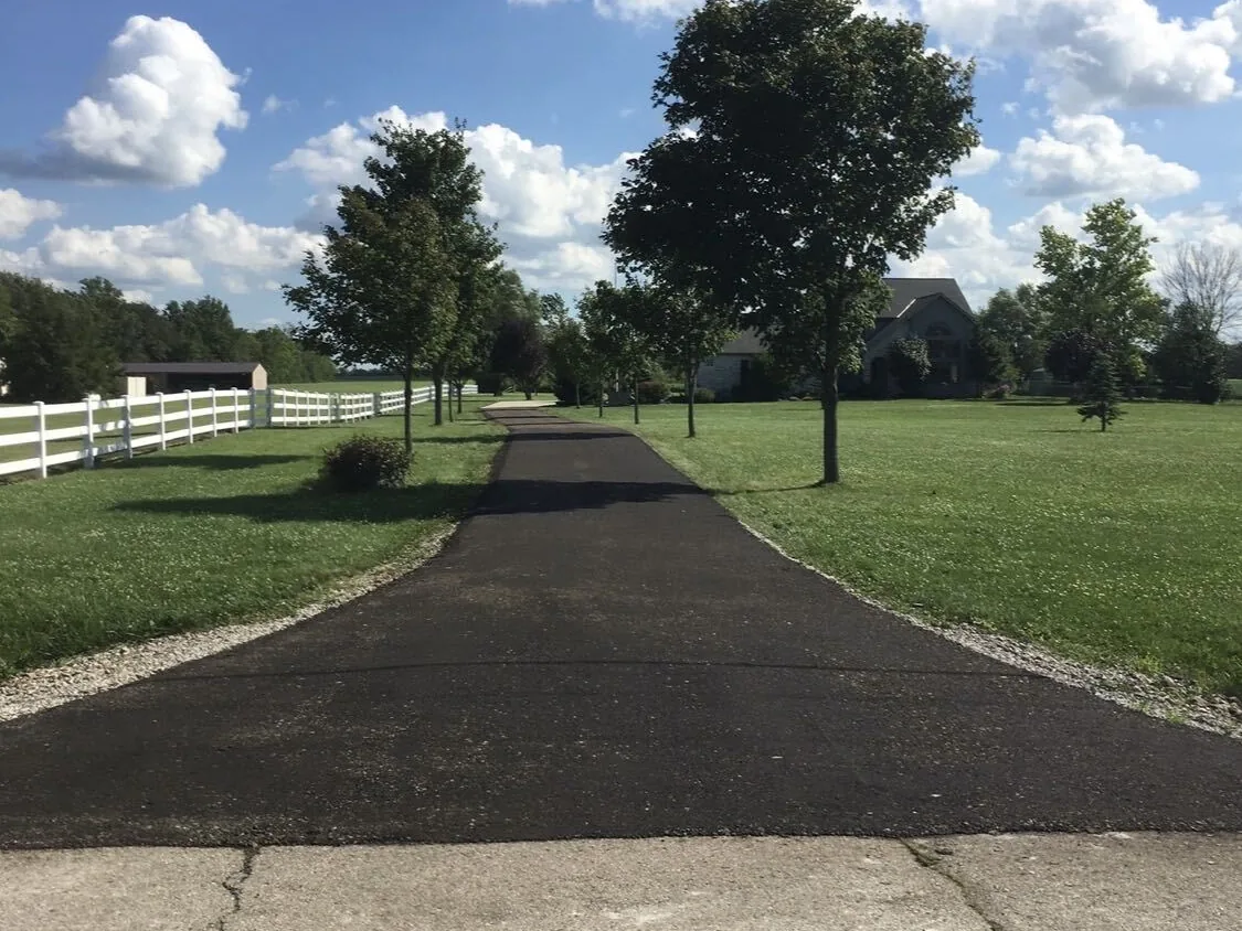 Long paved drive lined with young trees beside a white fence, private road paving