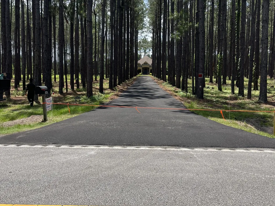 Long paved private drive through tall pines leading to a home, private road paving