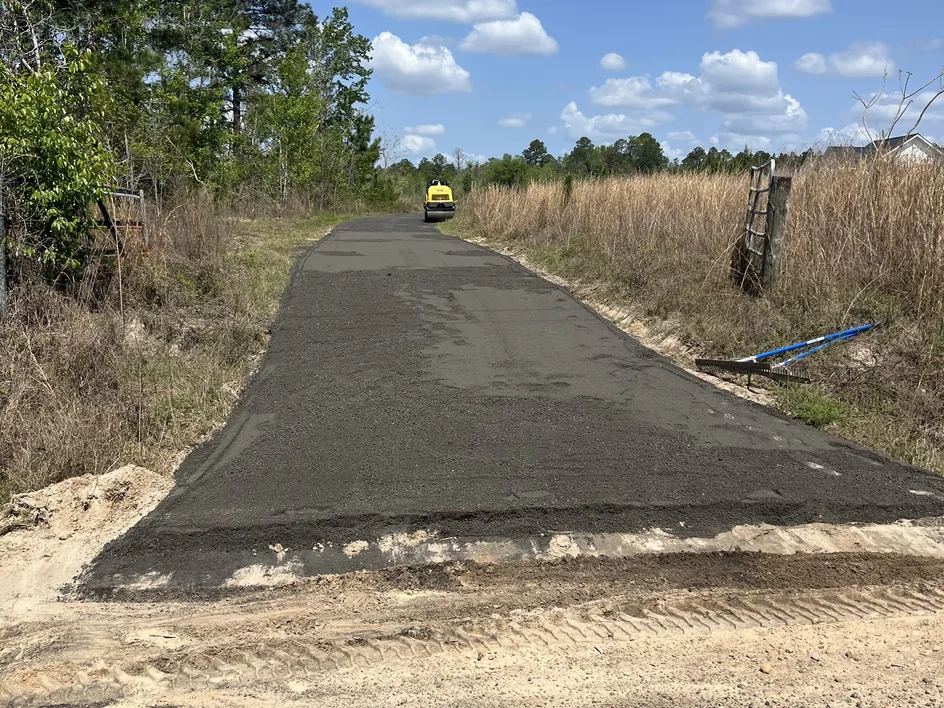 Roller compacting a new recycled asphalt lane through tall grass, private road paving