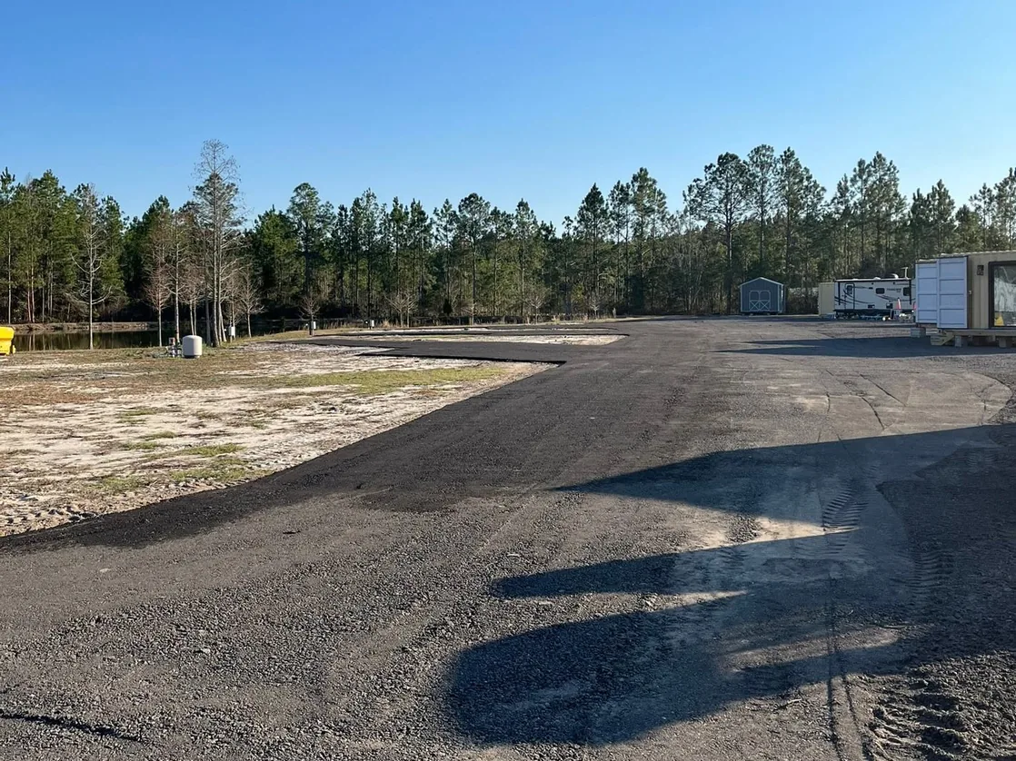 Freshly laid recycled asphalt millings lot and drive on sandy ground ringed by pines