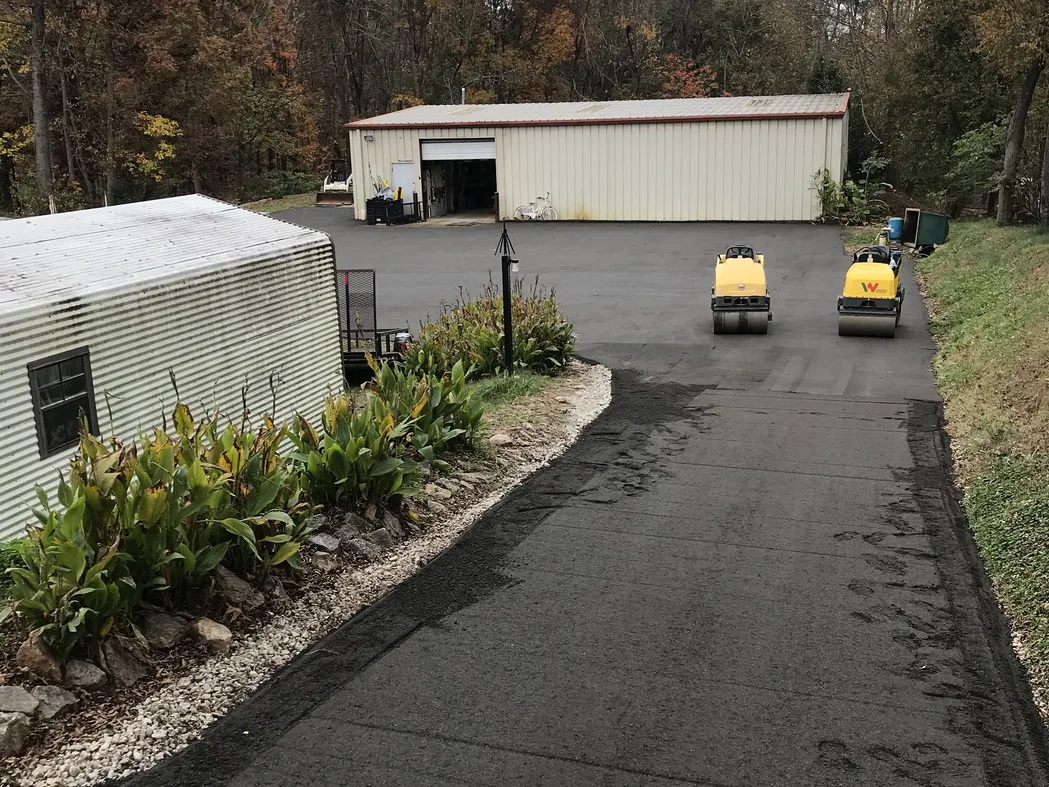 Two rollers on a freshly rolled recycled asphalt drive leading to a metal shop building