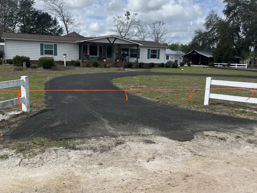 Freshly paved drive curving past white fence posts to a home, before any sealcoating