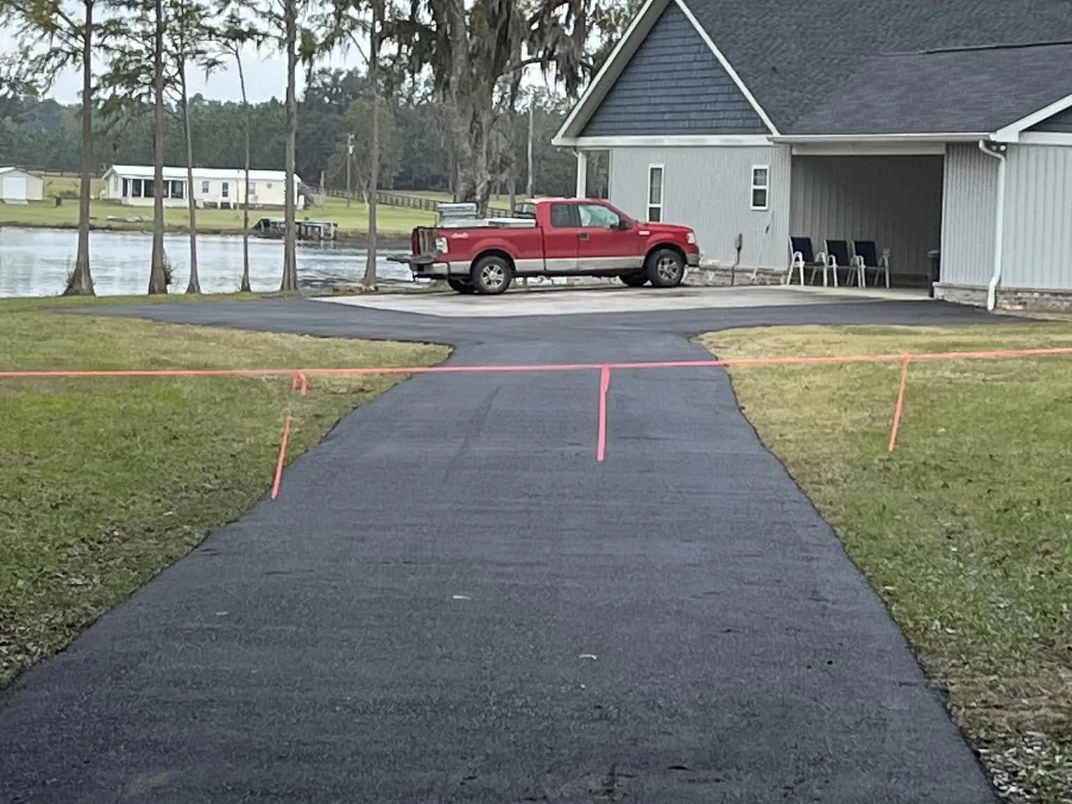 Freshly paved drive leading to a gray home by a pond, before any sealcoating